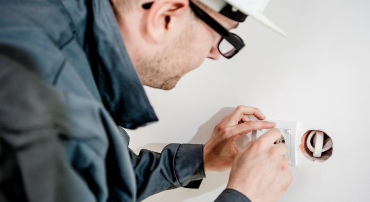 An electrician in a white hard hat and glasses installing a wall outlet
