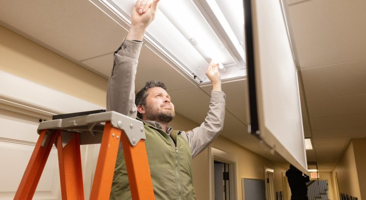 A man standing on an orange stepladder replacing a ceiling light fixture