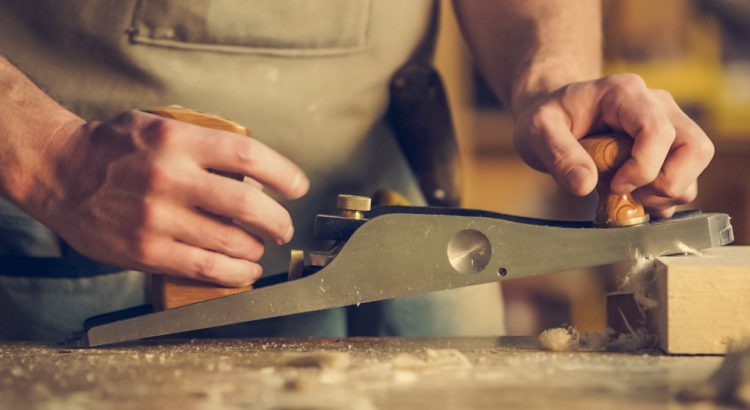 Close-up of a carpenter's hands pushing a hand plane across a piece of wood