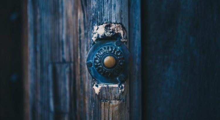 An old metal doorbell button on a weathered blue wooden door